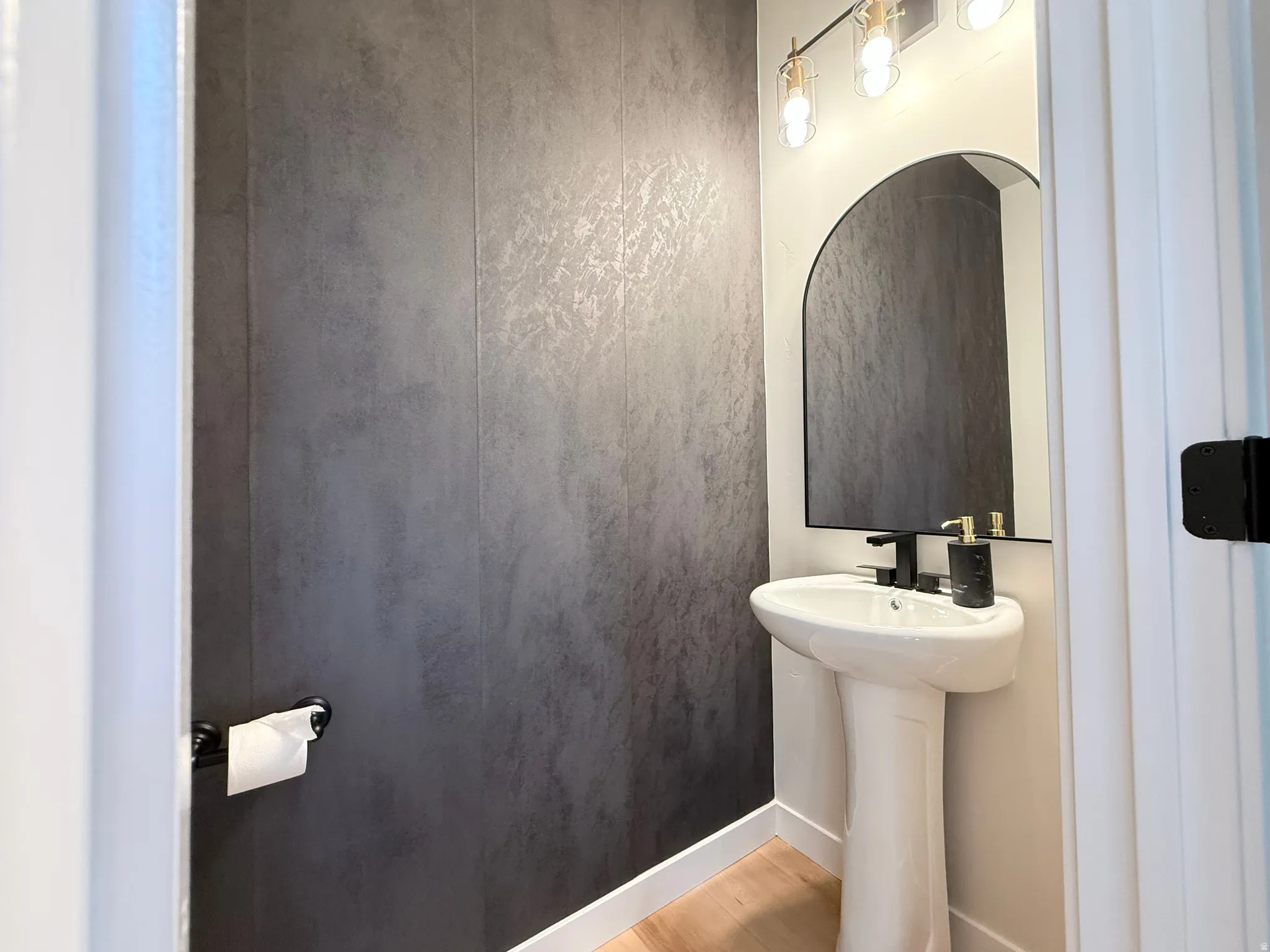 Pedestal sink with a matte black faucet, illuminated by a three-light vanity fixture