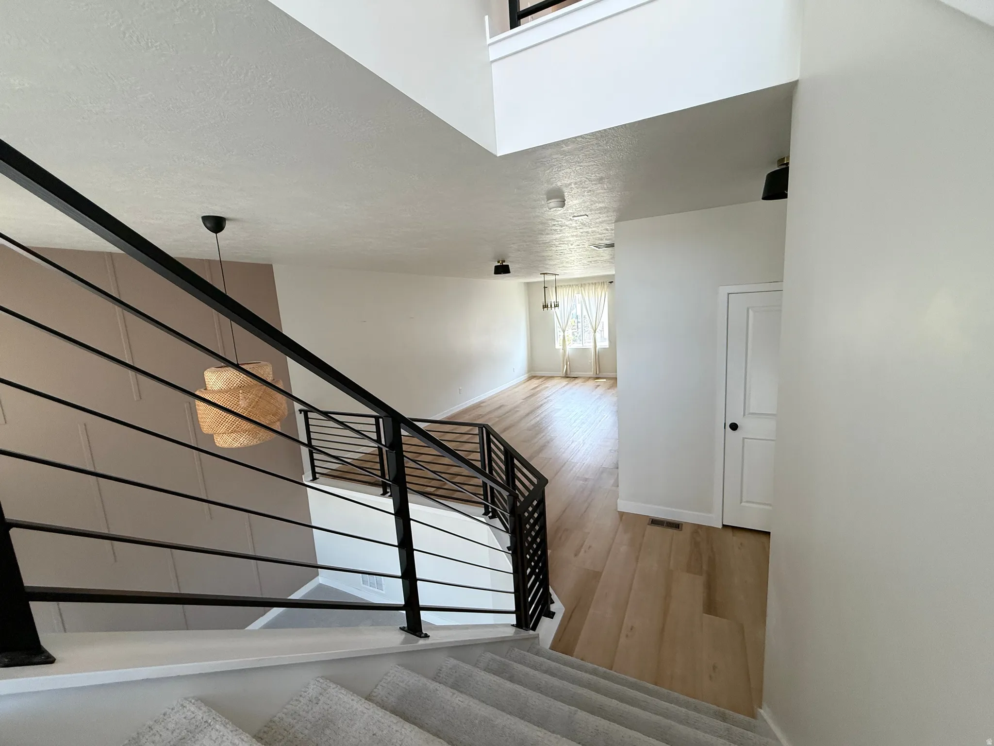 Open concept living space featuring wood-finish flooring, a modern black metal railing, and a textured accent wall
