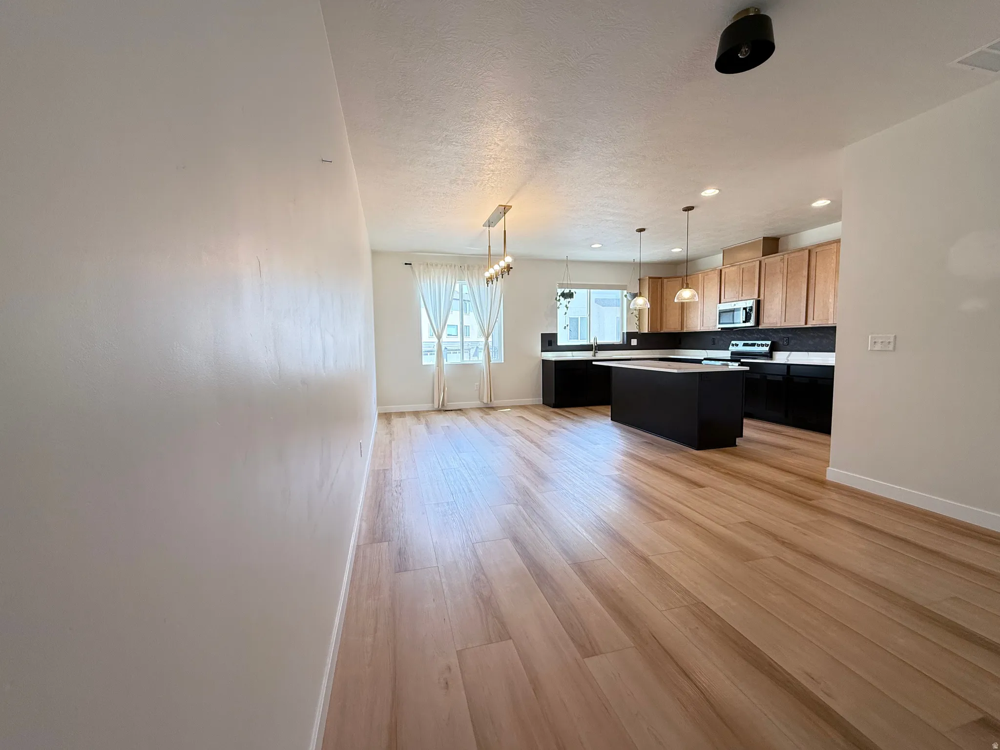 Light wood-finish flooring throughout, kitchen with dark island and light countertops, stainless steel appliances, and a tiled backsplash