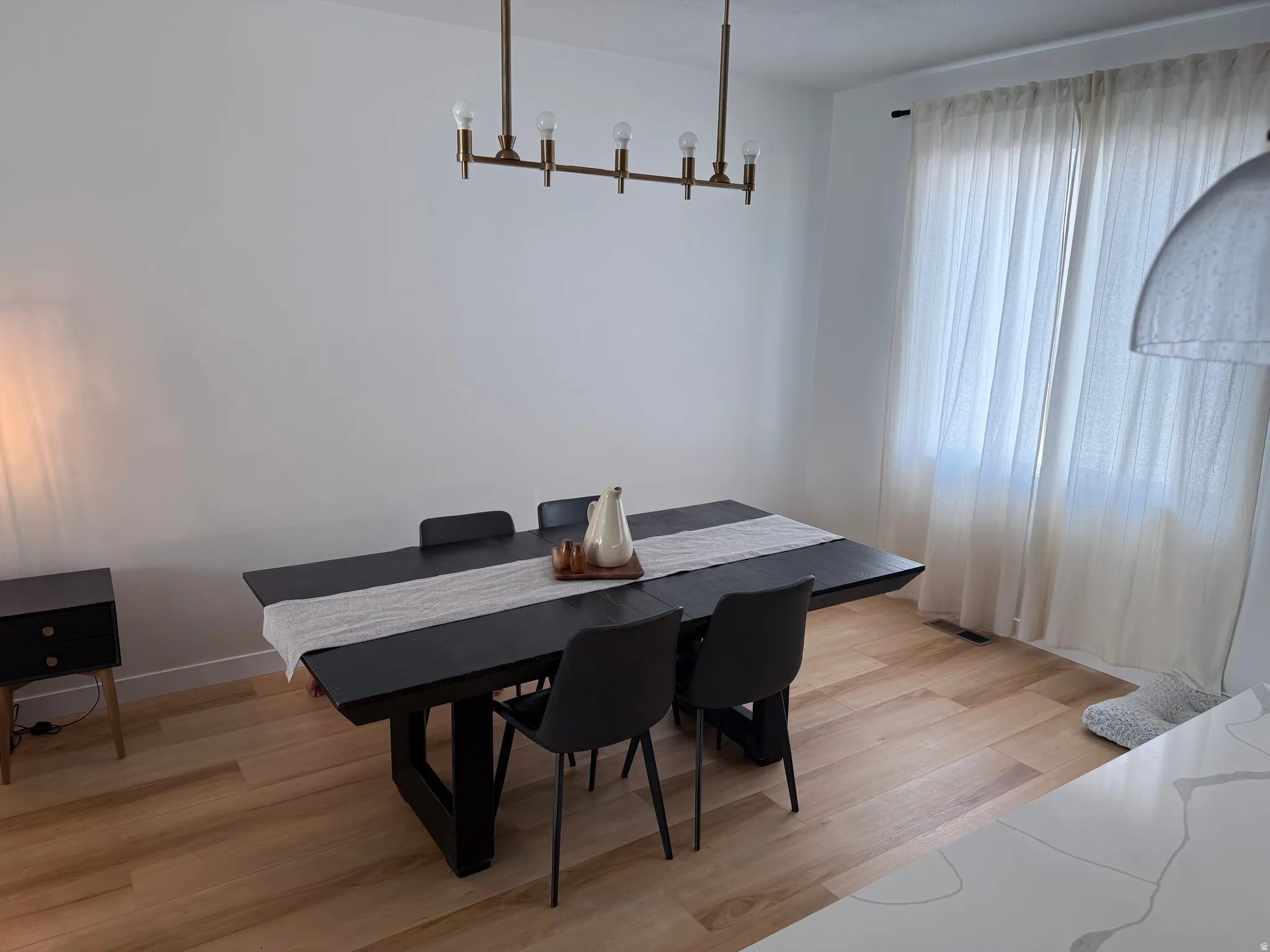 Dining area featuring light wood-finish flooring, a modern linear chandelier, and a large window with privacy curtains