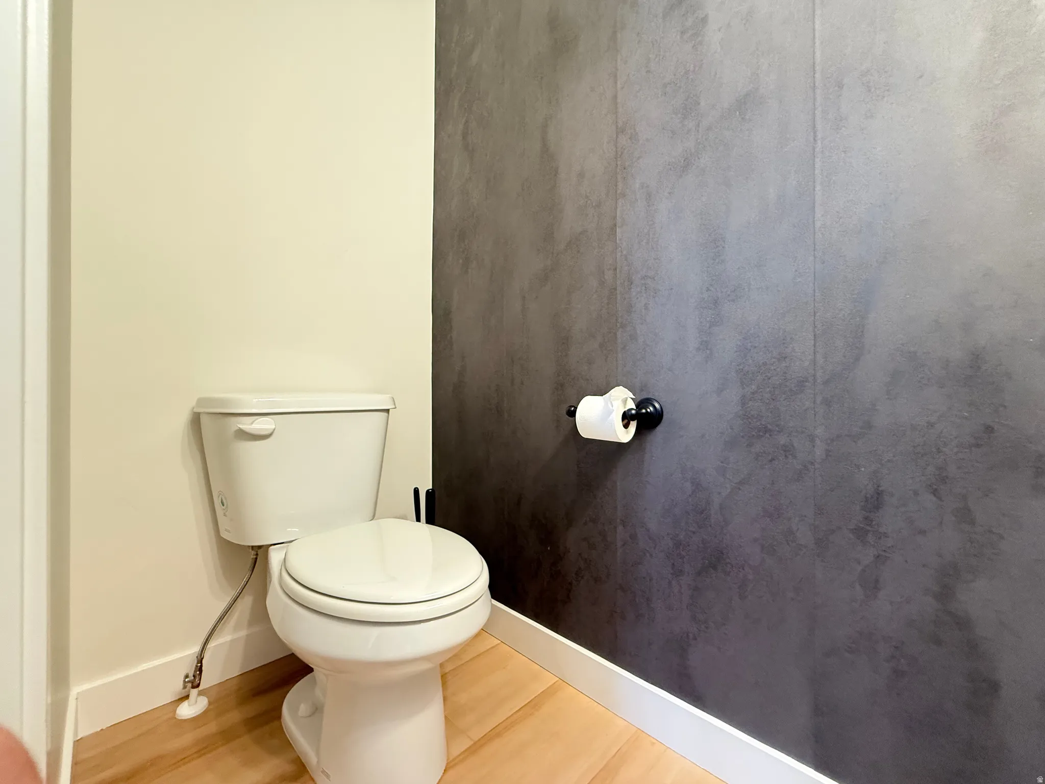 Light wood-finish flooring, white baseboards, and a white toilet