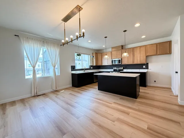 Open-concept kitchen and dining area featuring wood-finish flooring, a linear chandelier, a kitchen island with pendant lighting, and stainless steel appliances