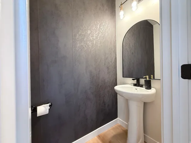 Pedestal sink with matte black faucet, arched mirror, contemporary vanity light fixture, and wood-finish flooring
