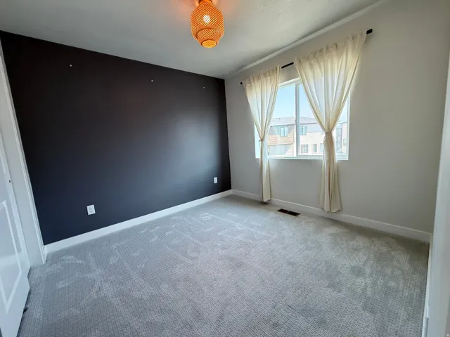 Carpeted room with a dark accent wall, white trim, and a window