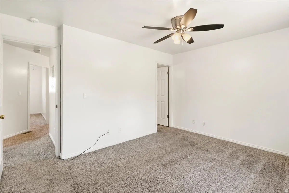 White-painted interior room with gray carpet flooring and a ceiling fan with brushed nickel accents