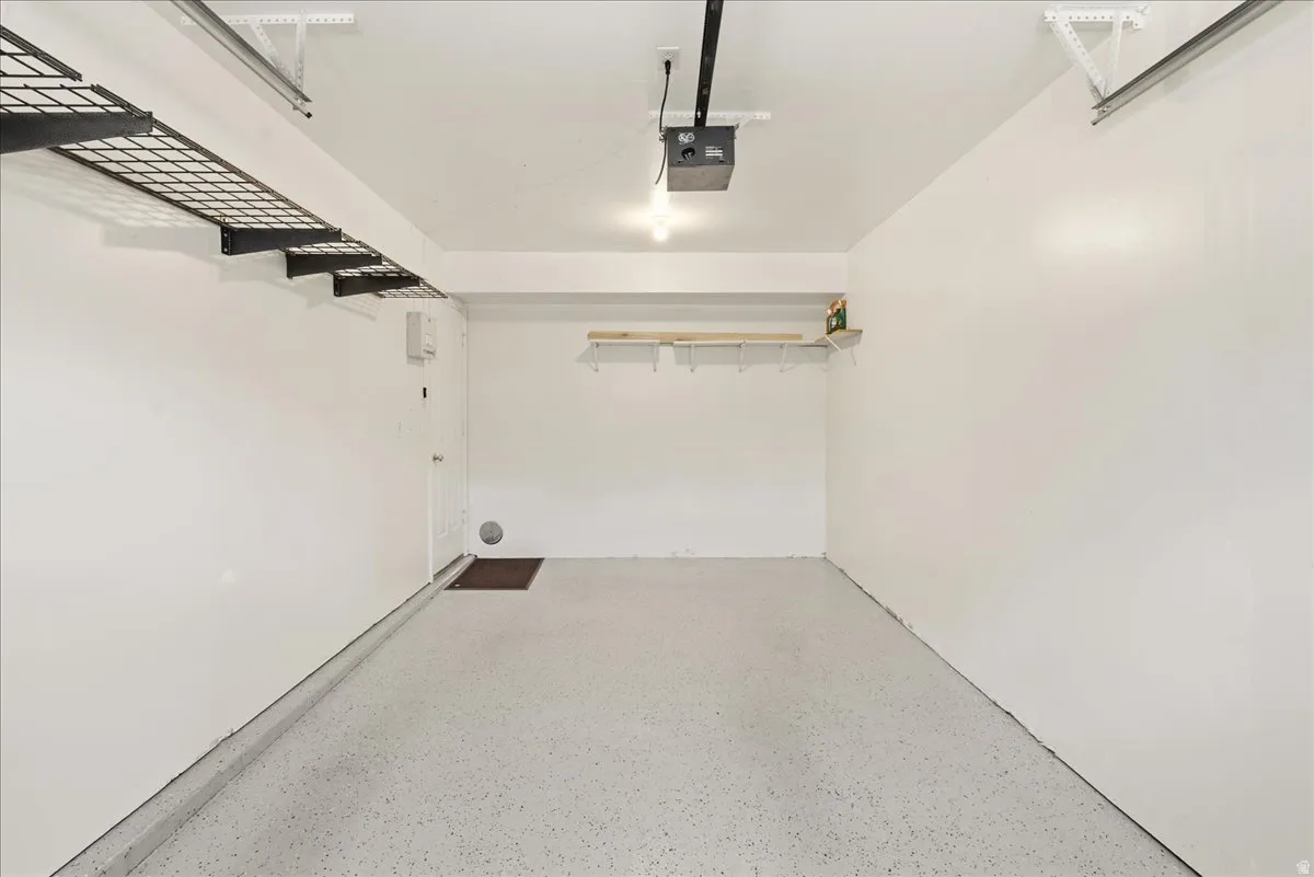 Bright garage space featuring a speckled epoxy floor coating, overhead storage racks, a wall-mounted shelving unit, and a standard entry door
