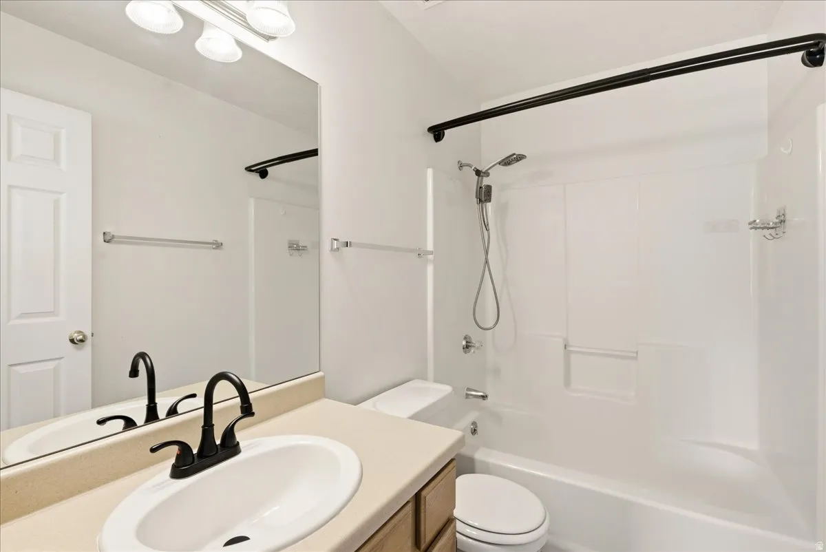 Bathroom featuring a tub/shower combination with white surround, a toilet, and a vanity with an integrated sink and matte black faucet
