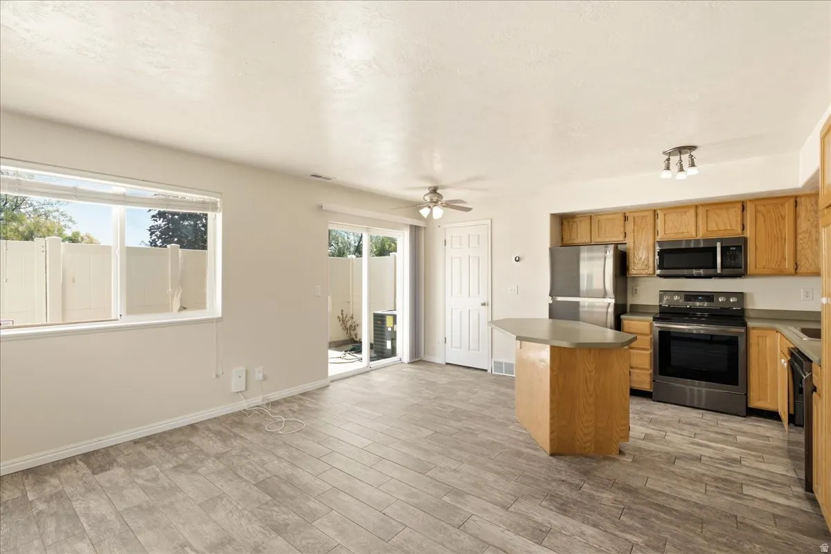 Open-concept living space featuring wood-finish flooring, a kitchen with stainless steel appliances, and light wood cabinetry