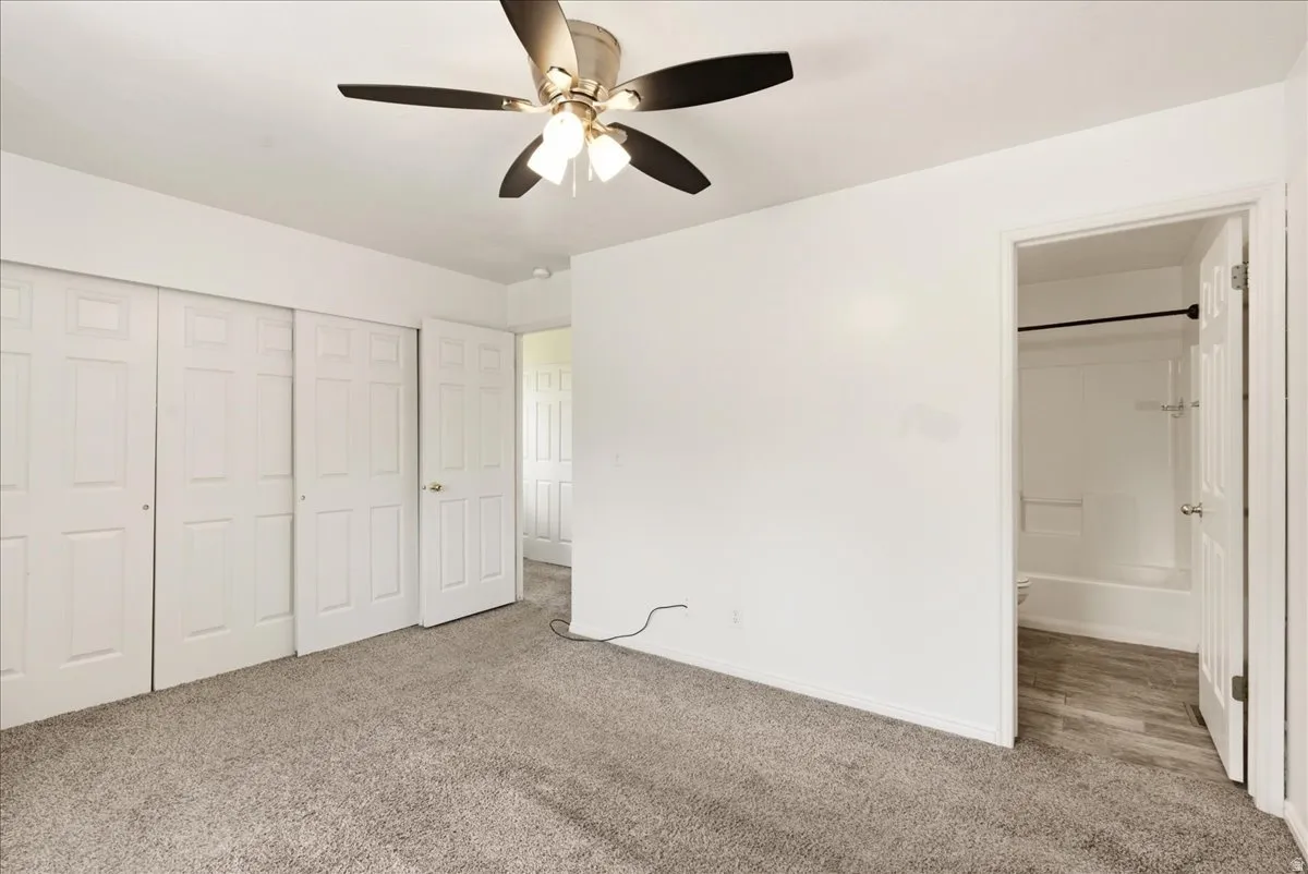 Carpeted room featuring a ceiling fan with integrated lighting, white walls, and bi-fold closet doors