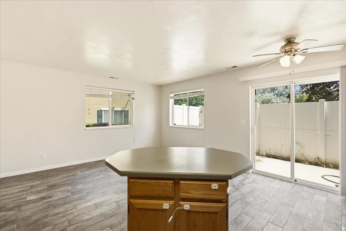 Kitchen island with wood cabinetry and countertop, wood-finish flooring, two windows with blinds, and a sliding glass door