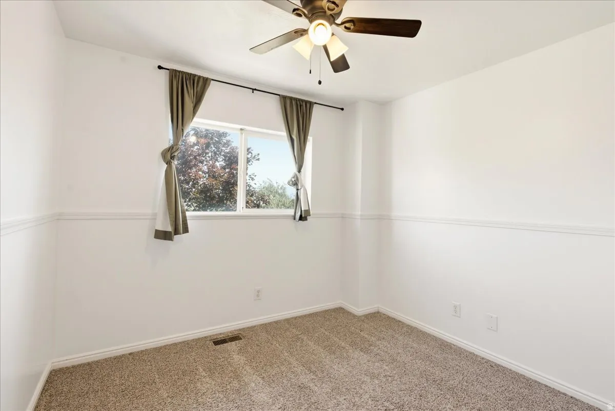 Carpeted room featuring a window with natural light, a ceiling fan with integrated lighting, white walls, and a decorative chair rail