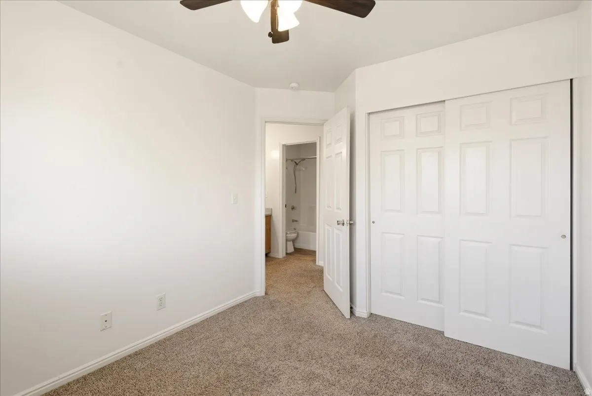 Carpeted room featuring a ceiling fan with light fixture, white trim, and a two-panel sliding closet door