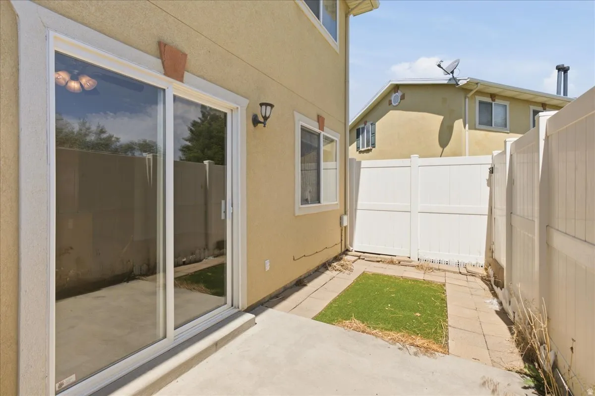 Patio area featuring a concrete surface, sliding glass door, exterior wall lighting, and a fenced perimeter