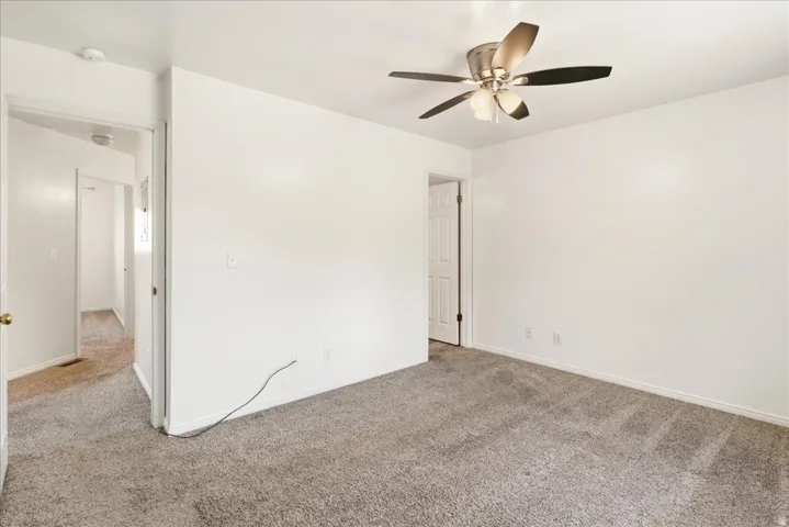 White-painted interior room with gray carpet flooring and a ceiling fan with brushed nickel accents