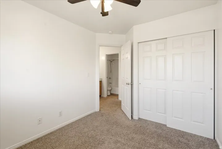 Carpeted room featuring a ceiling fan with light fixture, white trim, and a two-panel sliding closet door
