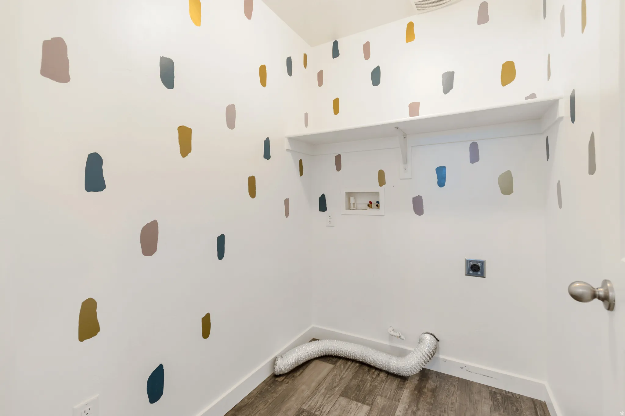 Laundry area featuring a built-in shelf, white baseboards, wood-finish flooring, and a decorative wall pattern