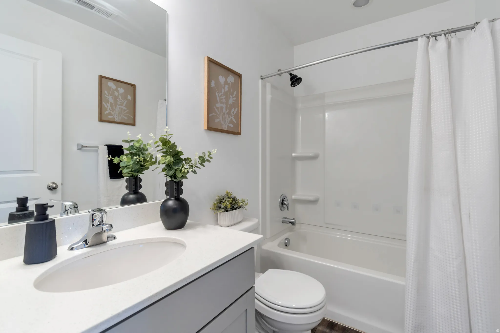 Bathroom featuring a white integrated tub and shower unit with a black shower head, a single vanity with a white countertop and undermount sink, and a white toilet