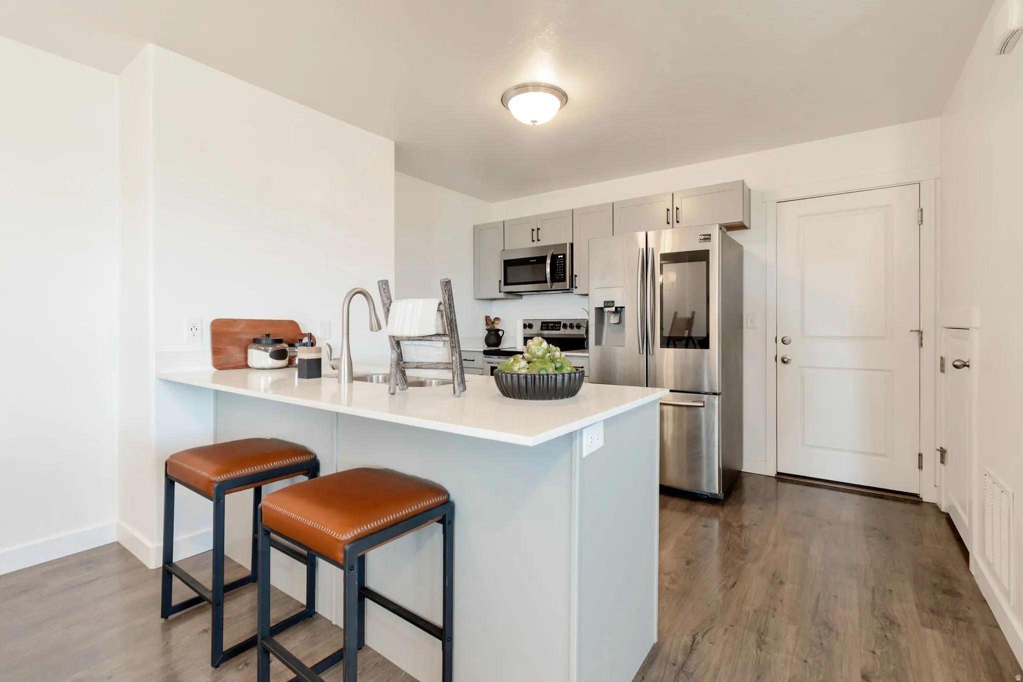 Contemporary kitchen featuring a light-toned countertop, integrated sink with a gooseneck faucet, stainless steel appliances, and sleek grey cabinetry
