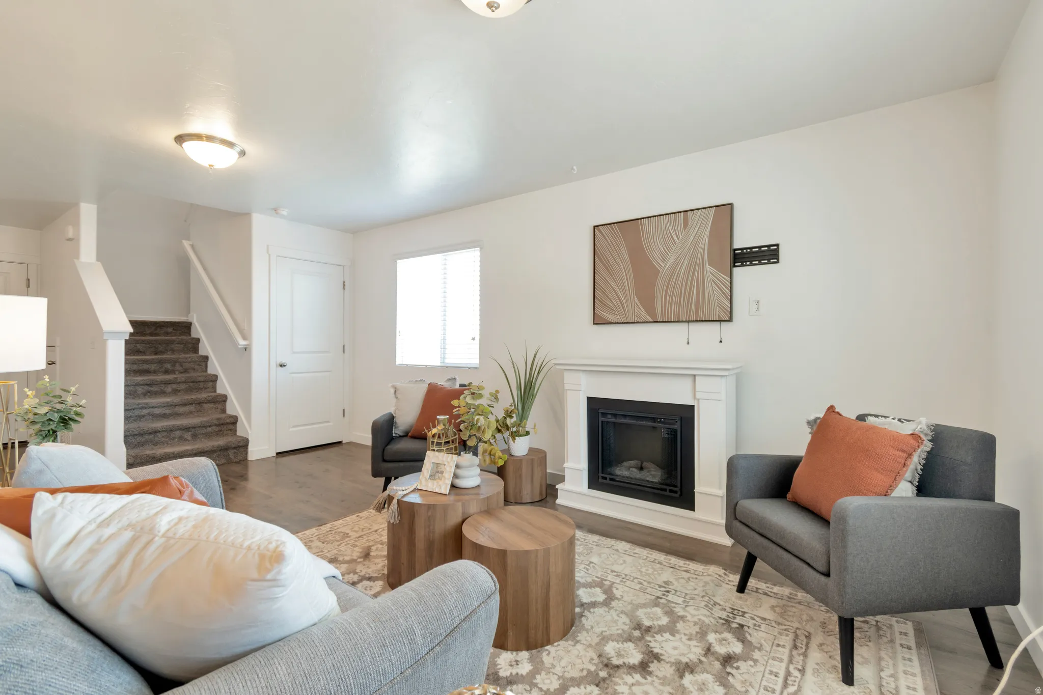 Living space featuring a white mantel fireplace, wood-finish flooring, and a window with blinds