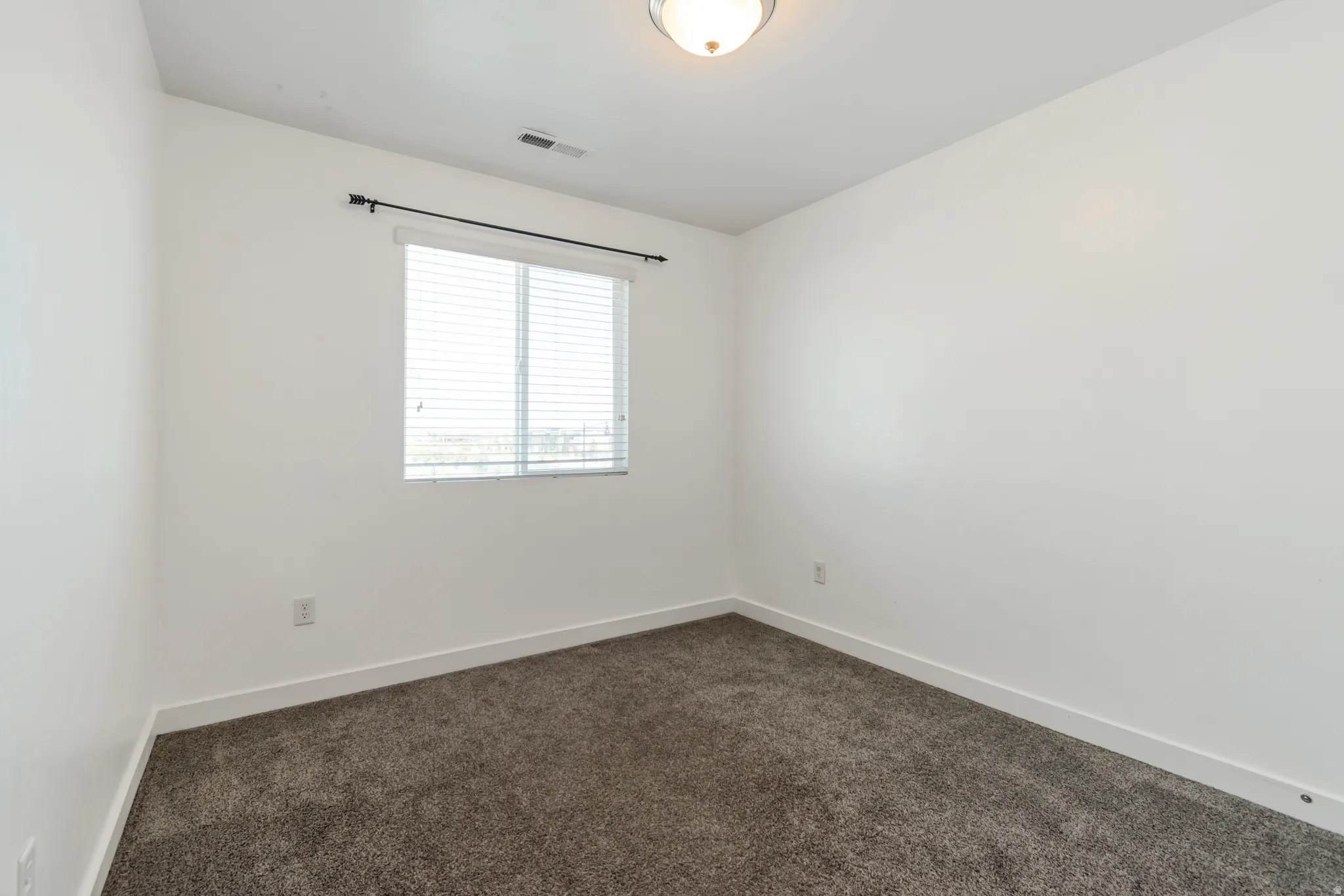 Room featuring a window with horizontal blinds, overhead lighting, white walls, white baseboards, and dark gray carpet