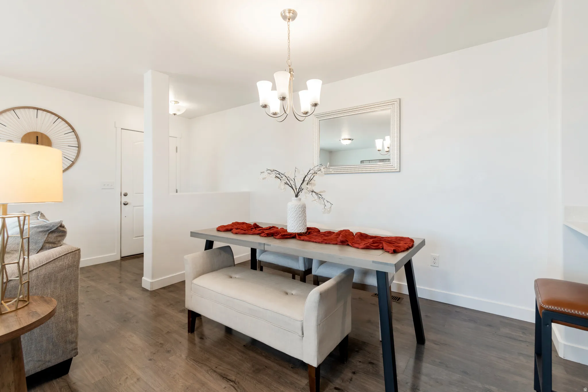 Open-concept living area featuring wood-finish flooring, a contemporary chandelier, and crisp white walls