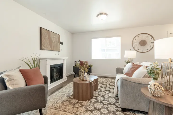 Living area featuring a fireplace with a white mantel, wood-finish flooring, and a single window with blinds