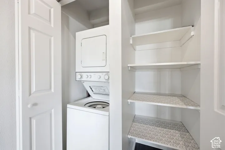 Dedicated laundry closet featuring a stacked washer and dryer, white paneled doors, and an adjacent storage pantry with built-in shelving