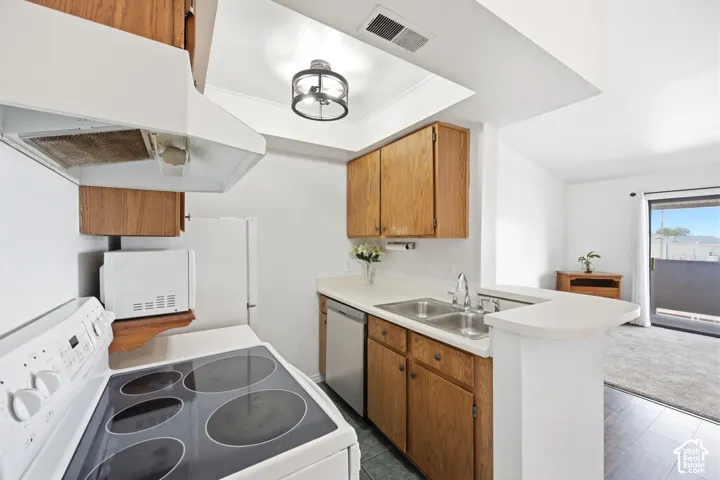 Kitchen featuring wood cabinetry, light-toned countertops, a double basin sink with a chrome faucet, a white electric range, and a stainless steel dishwasher