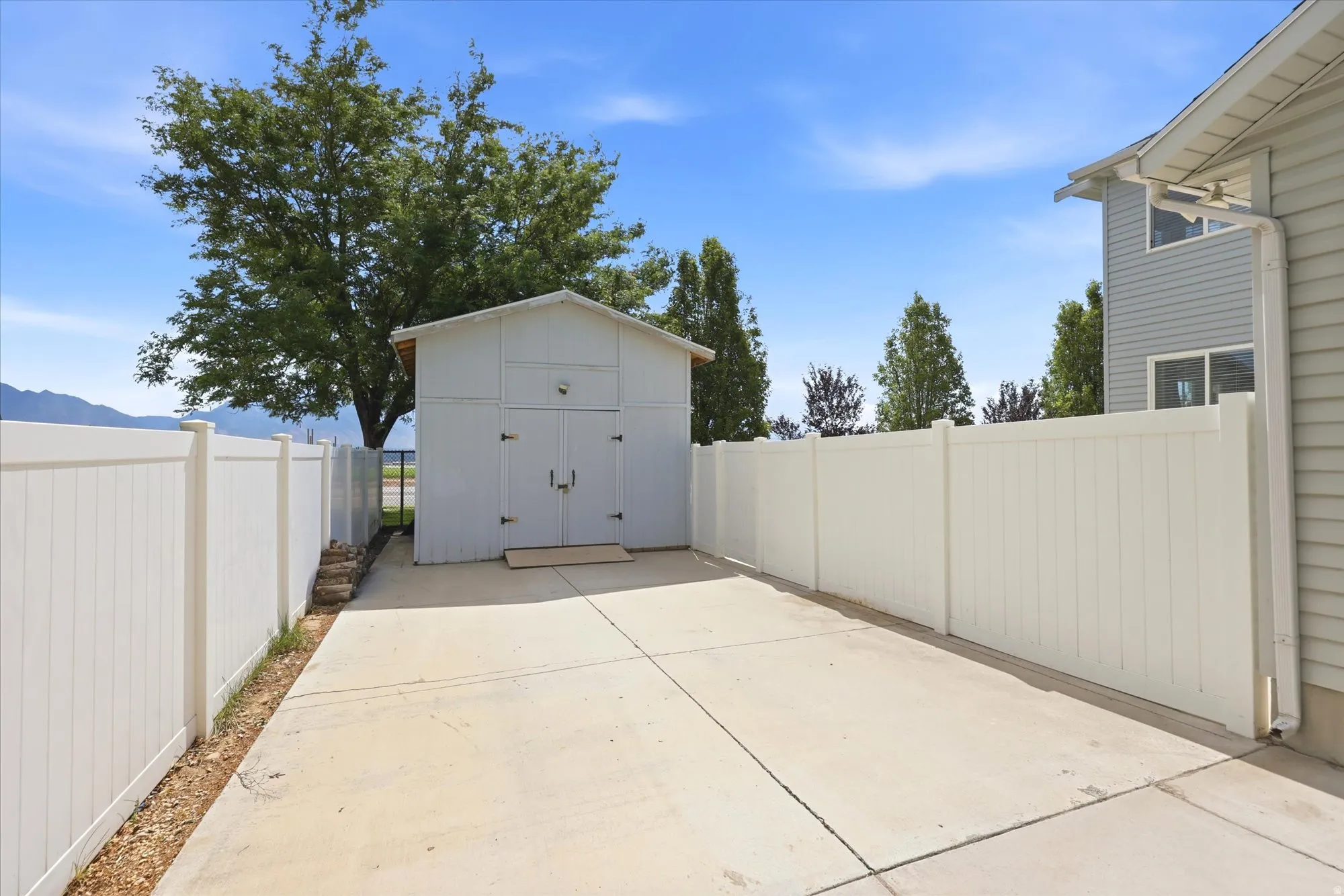 Paved concrete driveway with a freestanding storage shed, framed by a white privacy fence