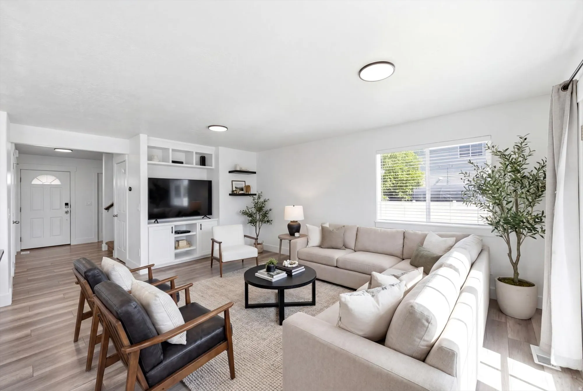 Open-concept living area with wood-finish flooring, a white trim entry door featuring an arched window, and a built-in media console with open shelving