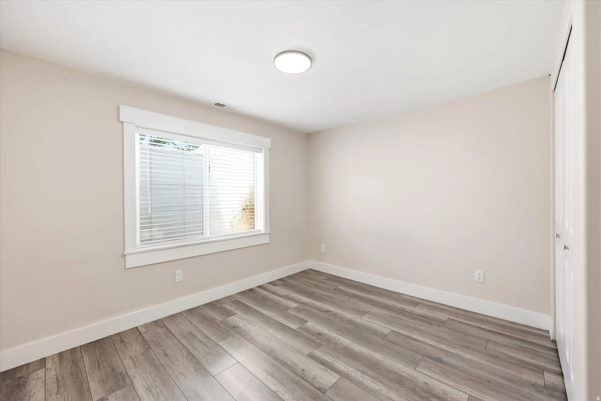 Room featuring wood-finish flooring, a double window with blinds, and white trim