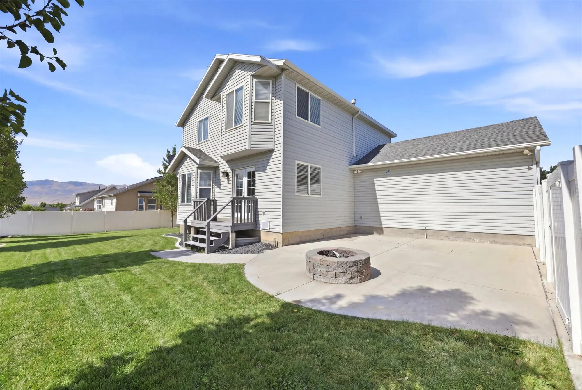 Expansive rear yard featuring a manicured lawn, concrete patio, and a built-in stone fire pit