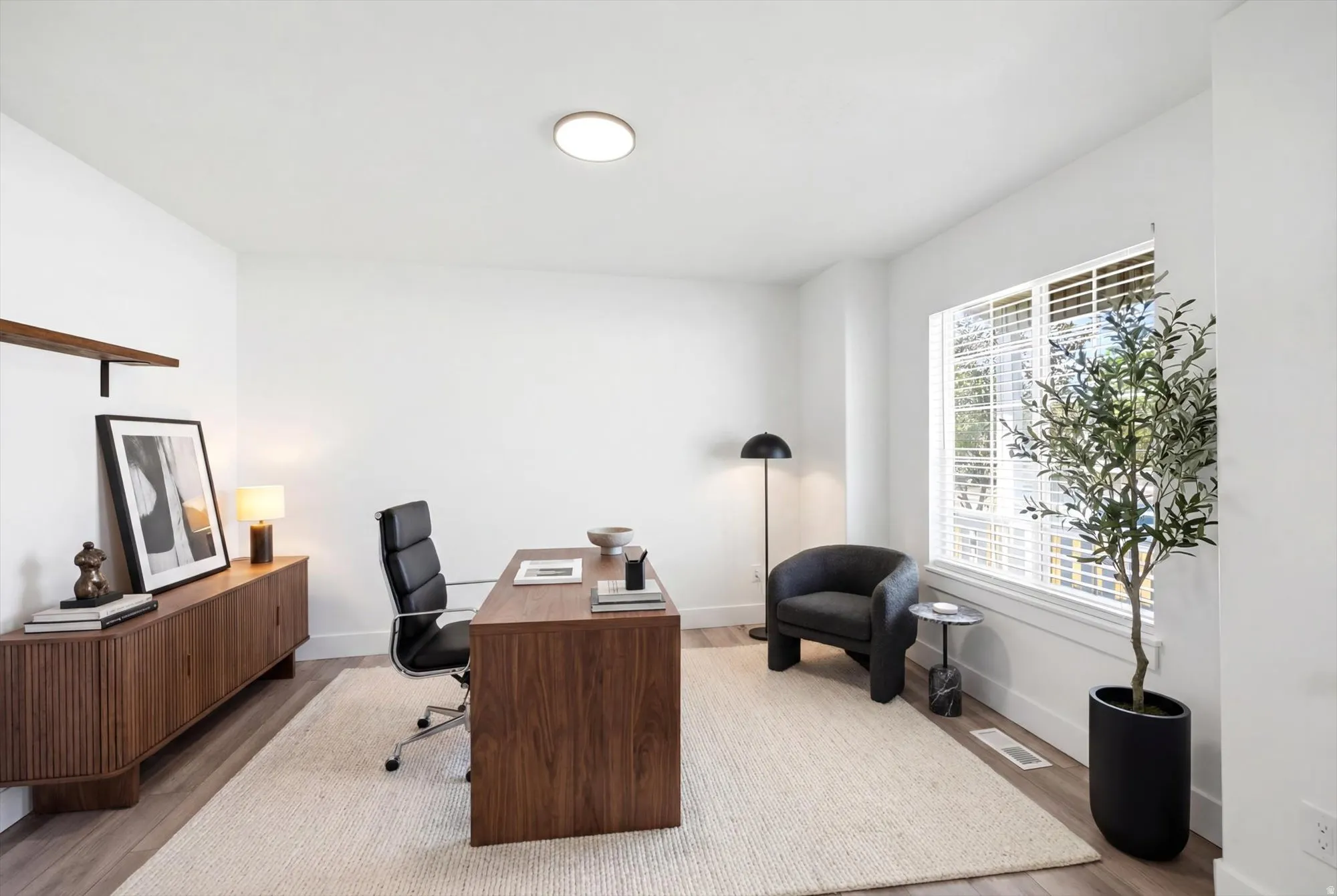 Bright room featuring wood-finish flooring, a large window with white blinds, and a built-in floating wood shelf