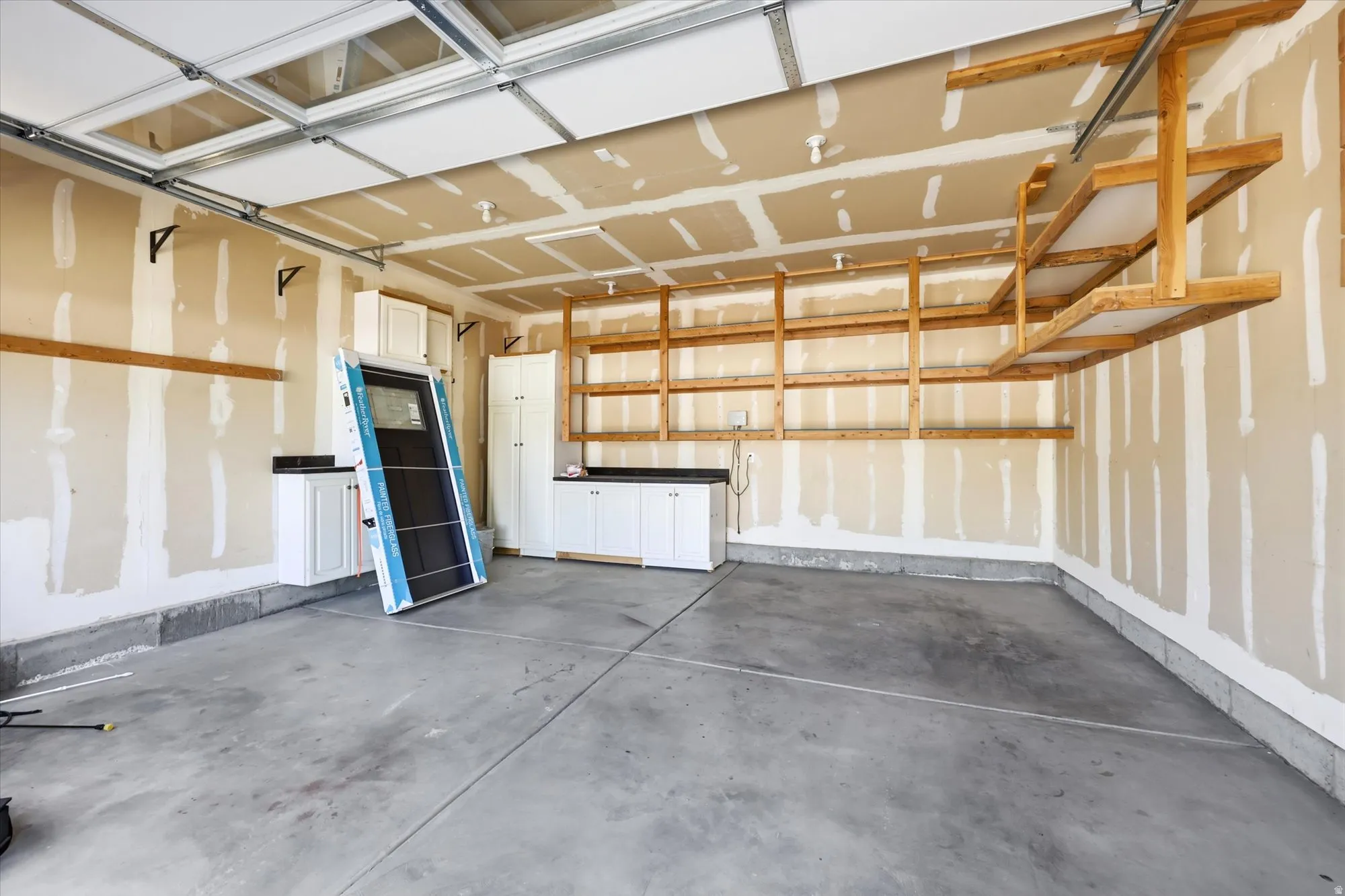 Spacious garage featuring a concrete floor, overhead storage shelves, built-in cabinetry with dark countertops, and a garage door with translucent panels
