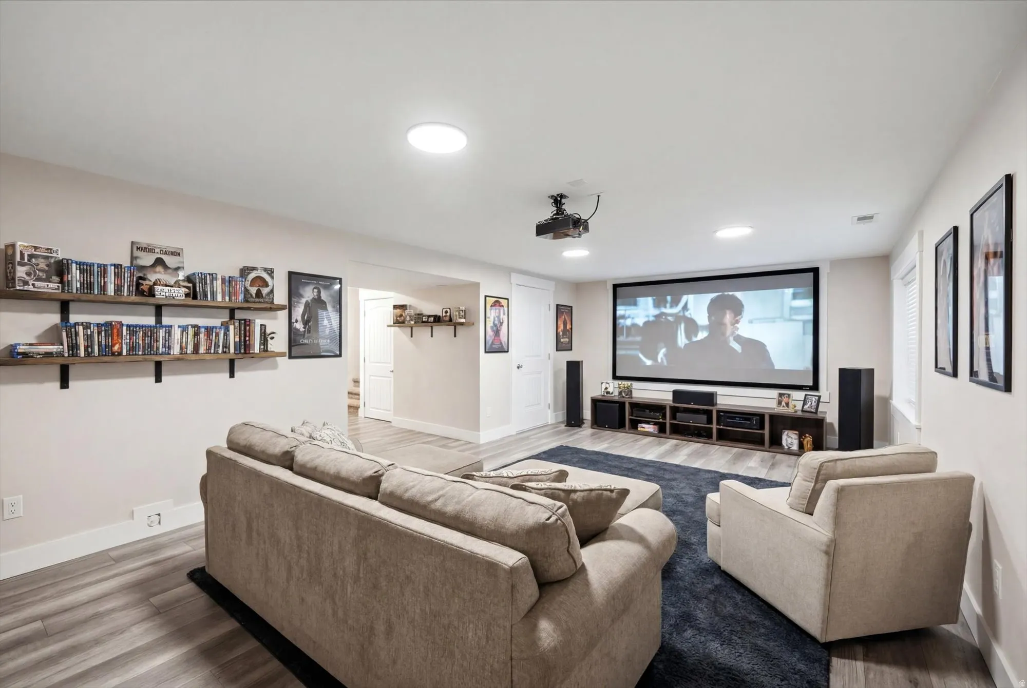 Dedicated media room featuring a large projection screen, recessed lighting, and wood-finish flooring