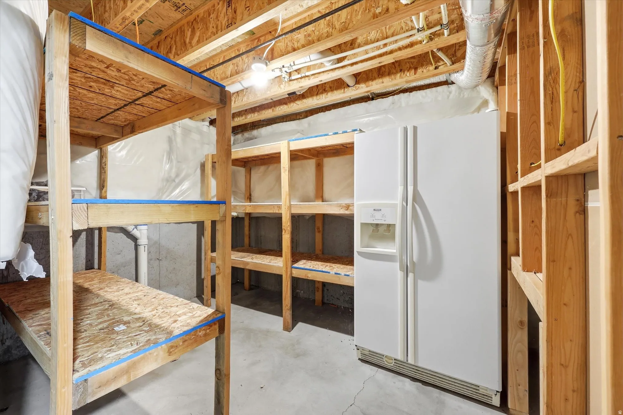 Unfinished basement space featuring exposed wood framing, concrete flooring, and built-in wood shelving units