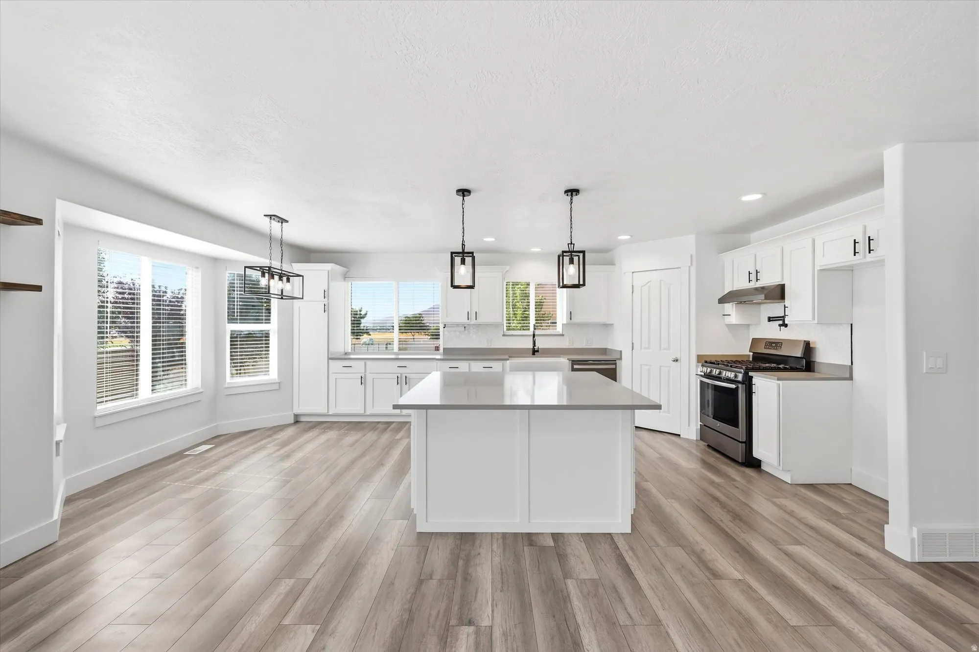 Open-concept kitchen featuring an expansive center island with a light-toned countertop, white cabinetry, integrated stainless steel appliances, and wood-finish flooring
