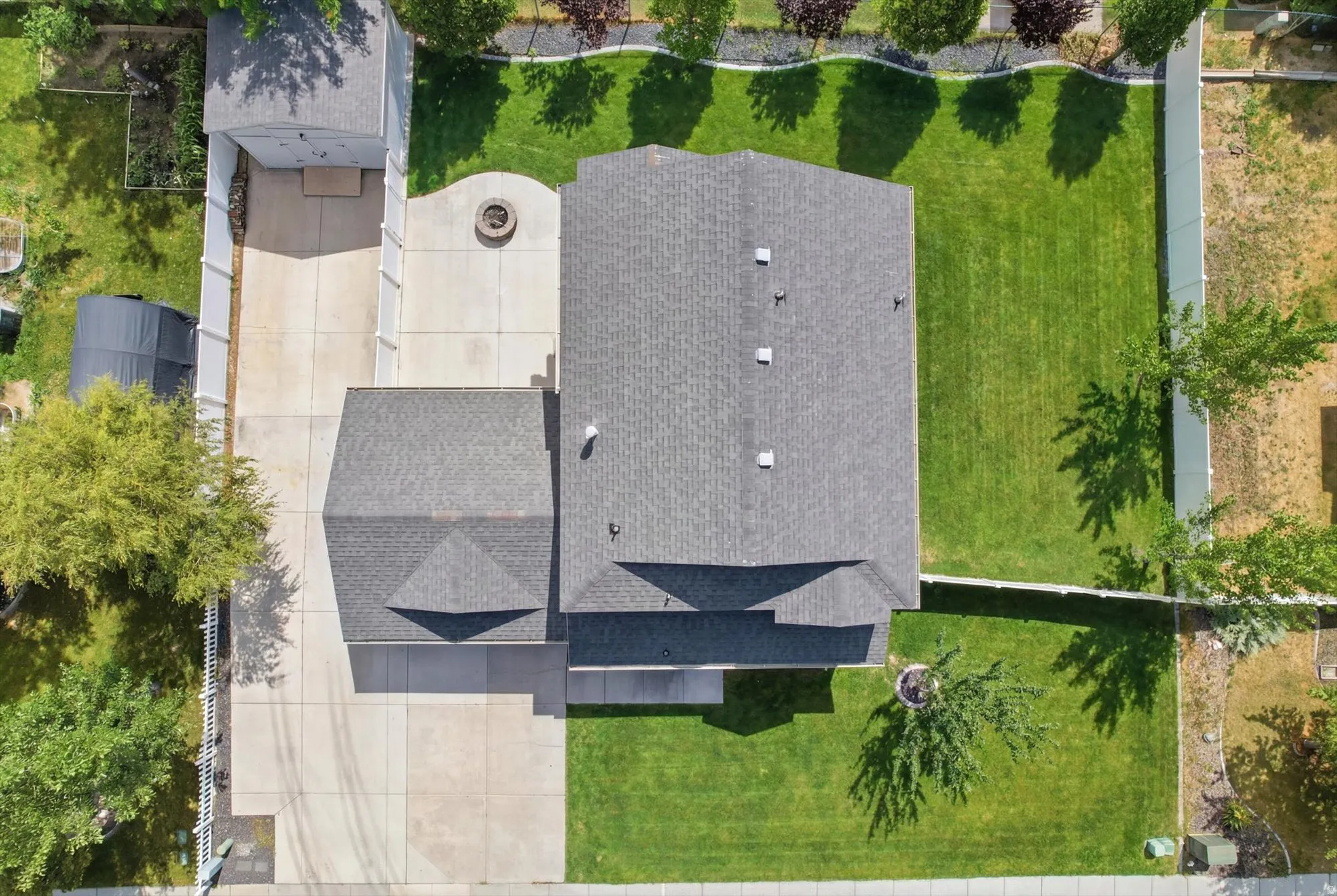 Aerial perspective highlighting a spacious backyard with a manicured lawn, paved patio featuring a built-in fire pit, and privacy fencing