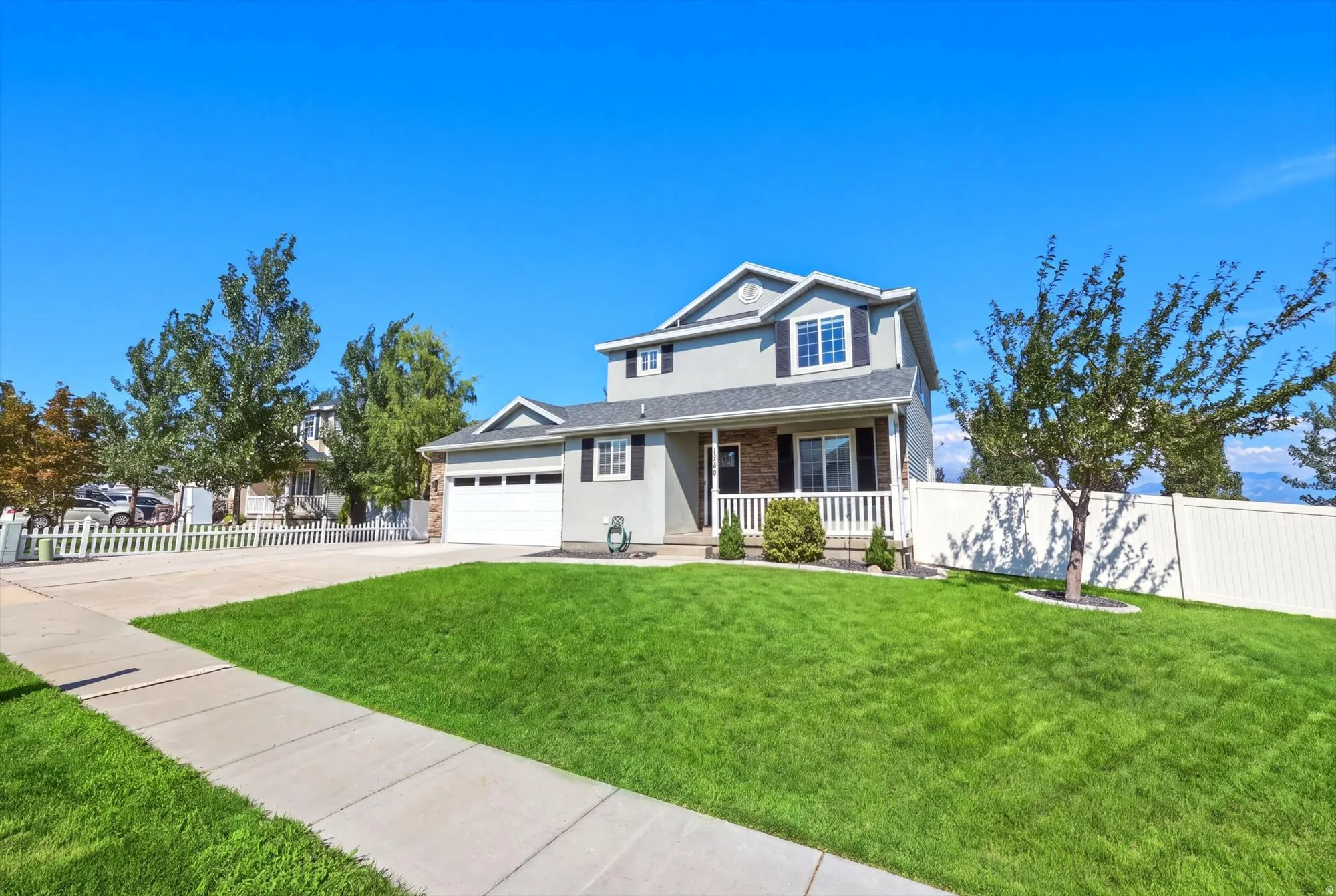 Two-story residence featuring a covered front porch, attached garage, and a lush green lawn