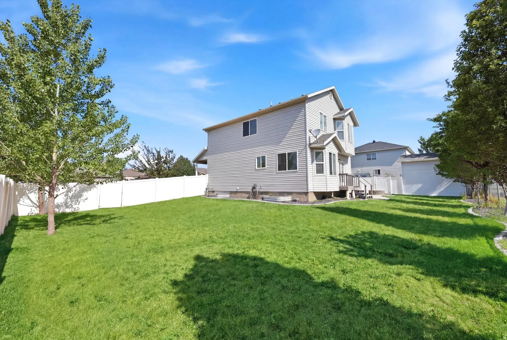 Expansive grassy backyard featuring a white privacy fence and established trees