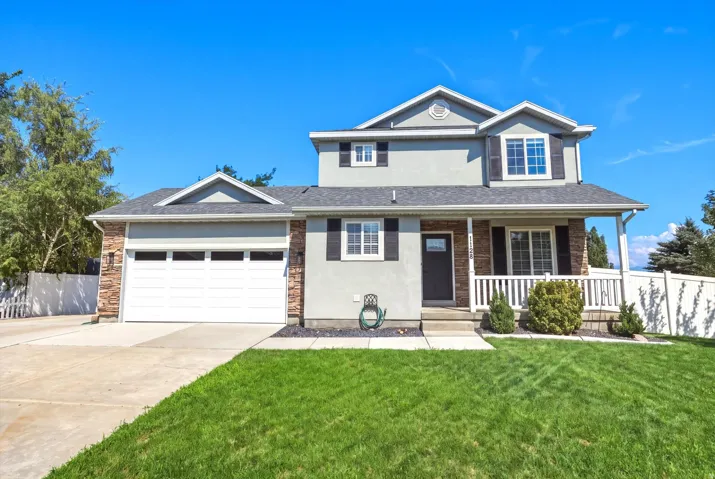 Two-story residence featuring a covered front porch with white railing, stone accents, and a two-car garage