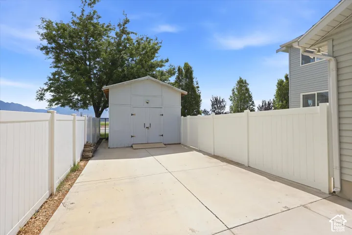 Paved concrete driveway with a freestanding storage shed, framed by a white privacy fence