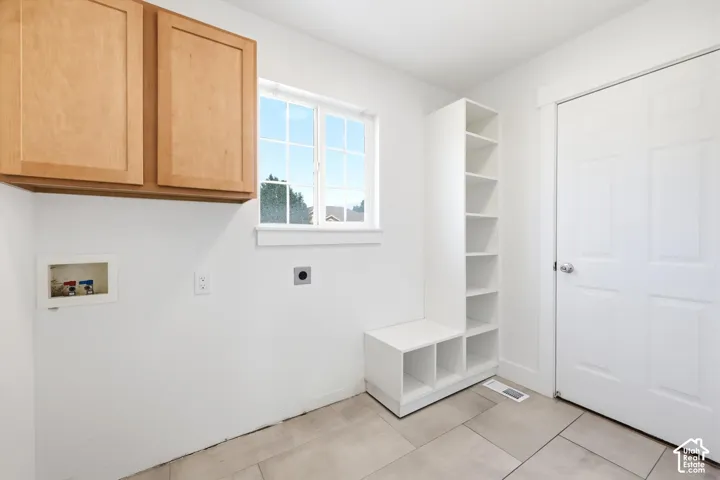 Laundry area featuring light wood-finish cabinetry, a window with grid panes, built-in open shelving, and neutral floor tiling