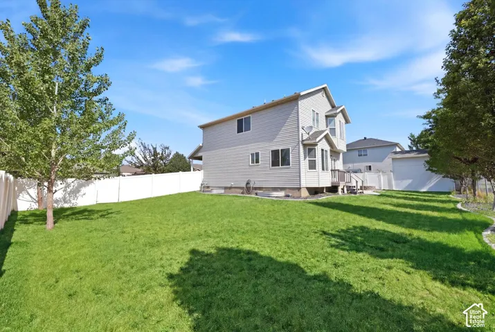 Expansive grassy backyard featuring a white privacy fence and established trees
