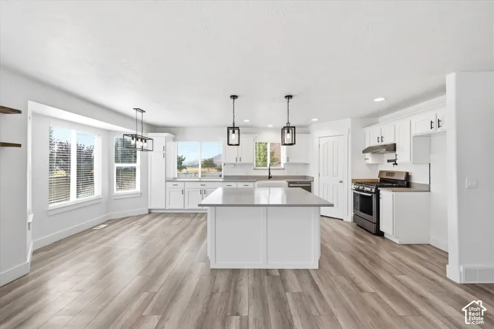 Open-concept kitchen featuring an expansive center island with a light-toned countertop, white cabinetry, integrated stainless steel appliances, and wood-finish flooring