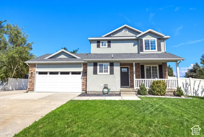 Two-story residence featuring a covered front porch with white railing, stone accents, and a two-car garage