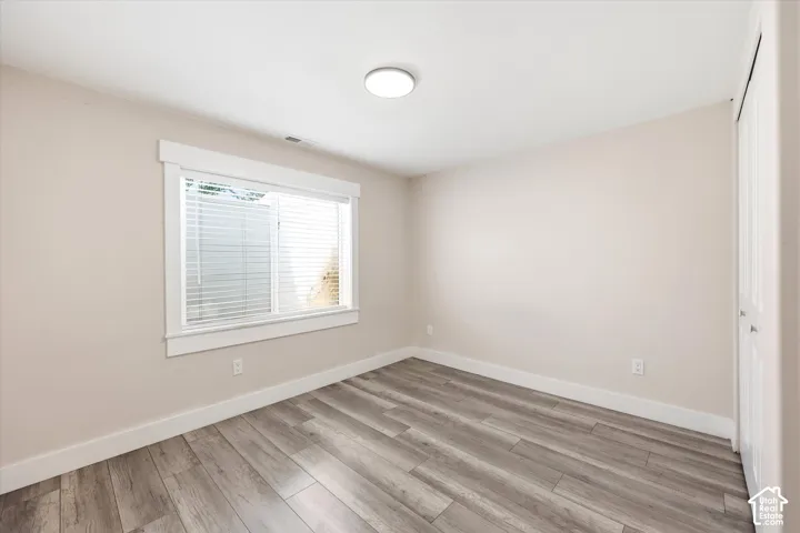 Room featuring wood-finish flooring, a double window with blinds, and white trim