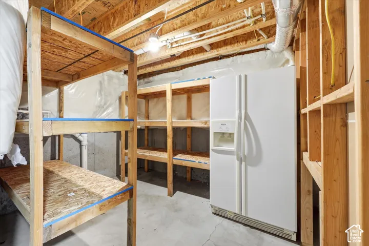 Unfinished basement space featuring exposed wood framing, concrete flooring, and built-in wood shelving units