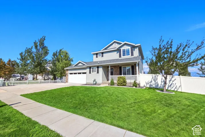 Two-story residence featuring a covered front porch, attached garage, and a lush green lawn