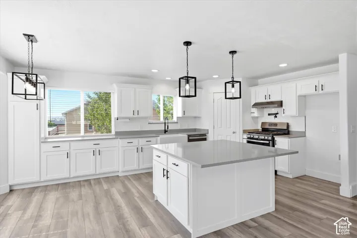 Bright kitchen with white cabinetry, wood-finish flooring, a central island with a light-colored countertop, and modern pendant lighting fixtures